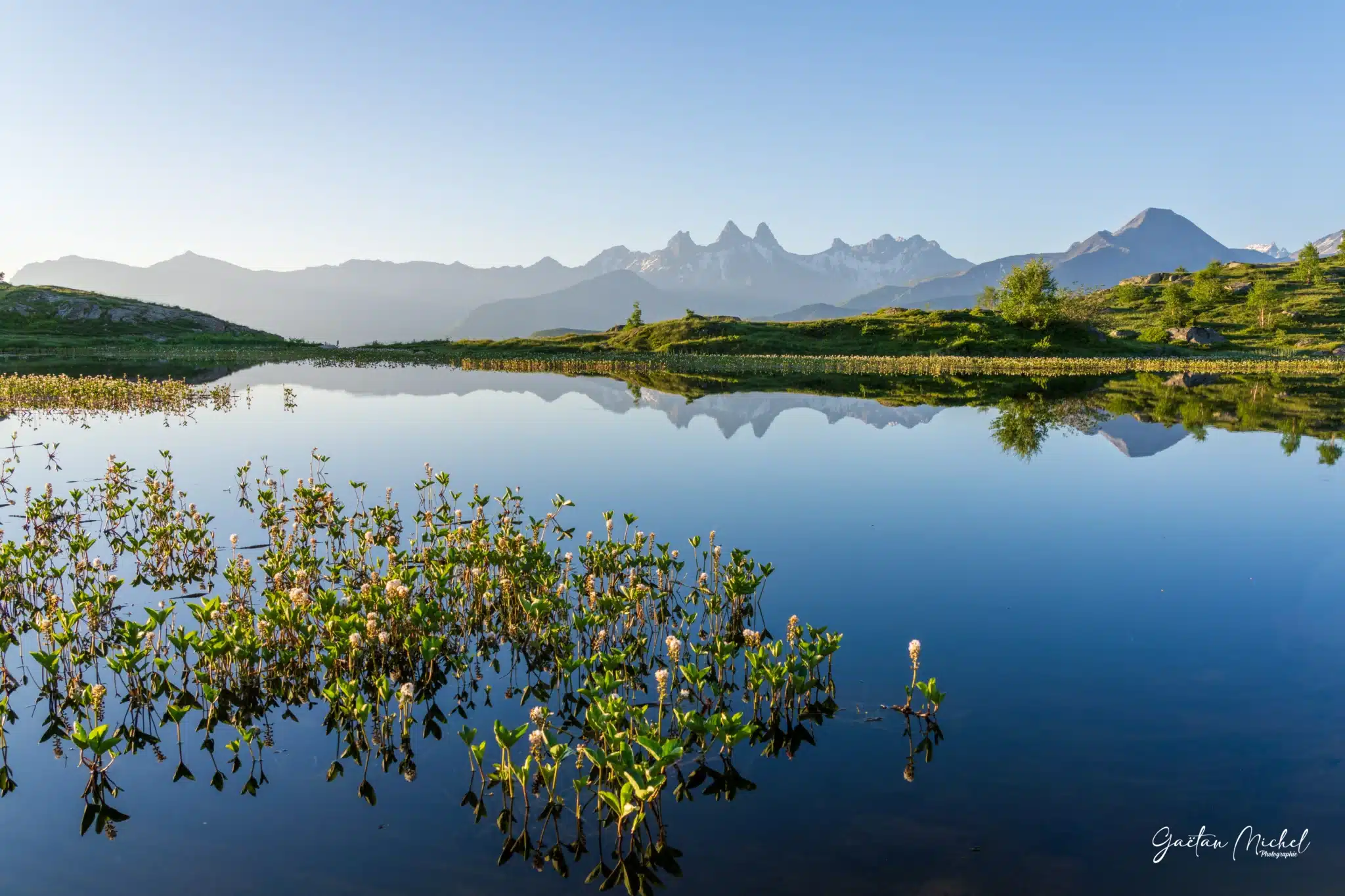 Au petit matin, les Aiguilles d’Arves se reflètent dans les eaux calmes du Lac Guichard, au Col de la Croix de Fer. Reflet des Aiguilles d’Arves dans le Lac Guichard au lever du jour, Col de la Croix de Fer