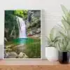 Tirage photo encadré d’une cascade dans le torrent de l’Alloix en Chartreuse, posé sur une étagère en bois clair. L’image montre une cascade avec une eau turquoise et des rochers moussus, entourée de végétation alpine. À côté, deux plantes vertes en pot (un aloe vera et une plante à larges feuilles) ajoutent une touche naturelle à la scène.