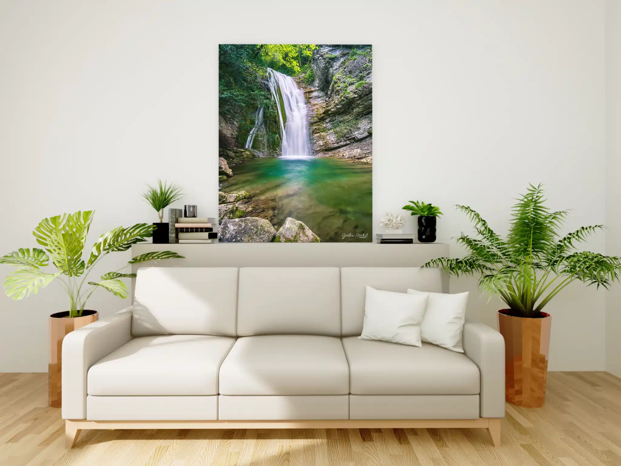 Tirage photo encadré d’une cascade dans le torrent de l’Alloix en Chartreuse, accroché au mur d’un salon moderne. L’image montre une cascade avec une eau turquoise s’écoulant entre des rochers moussus, entourée d’une forêt alpine. Le cadre est suspendu au-dessus d’un canapé blanc, entre deux plantes vertes en pot. Photo prise par Gaëtan Michel