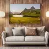 Tirage photo encadré d’un paysage alpin avec lac et montagnes, accroché au mur en bois clair d’un salon. En dessous, un canapé beige avec des coussins, deux lampes sur pied de chaque côté, et une petite table avec une plante verte.