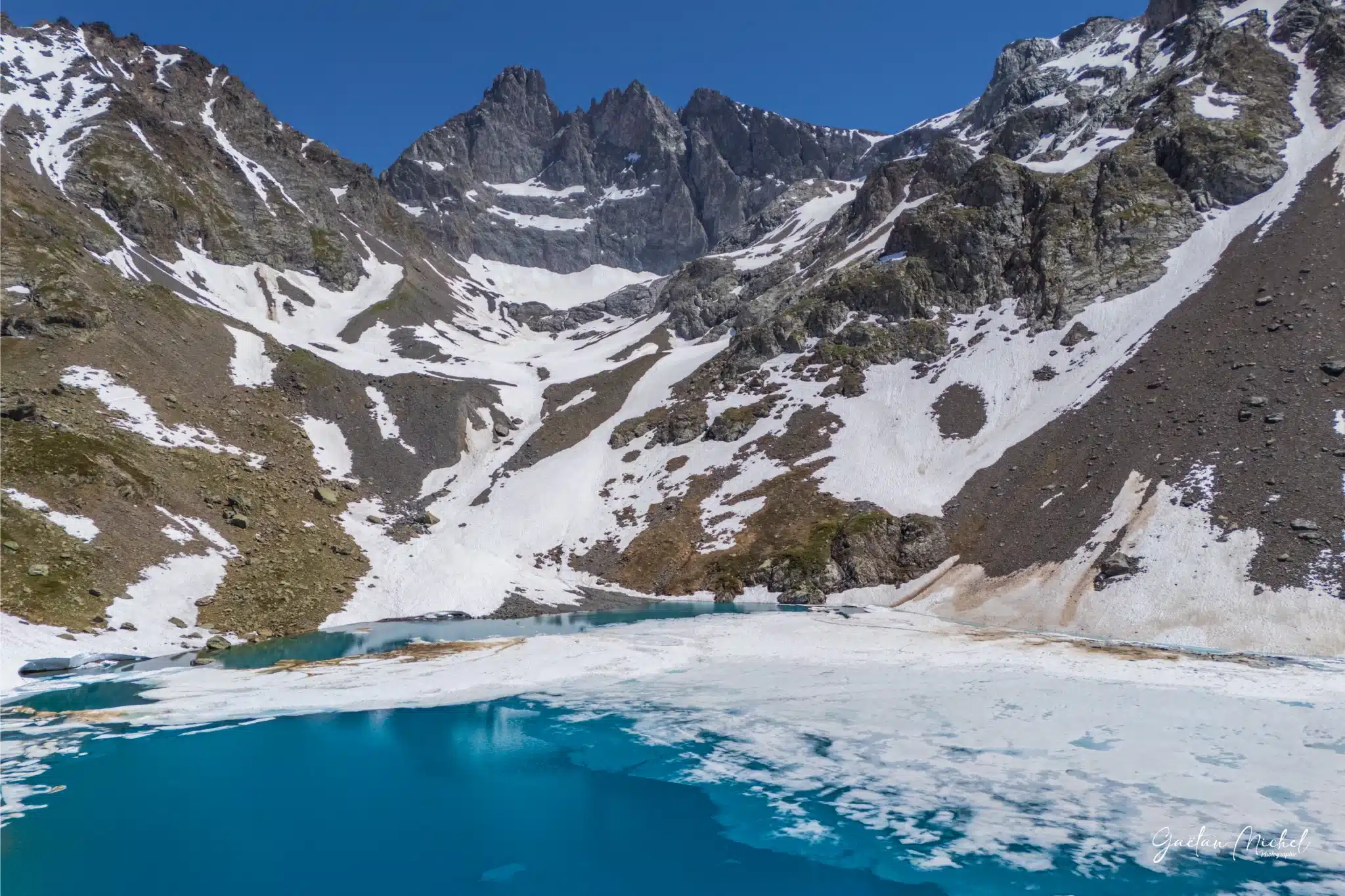 La débâcle printanière révèle les eaux turquoise du Lac Blanc de Belledonne au pied des sommets enneigés. Le Lac Blanc de Belledonne en période de débâcle, avec ses eaux turquoise émergeant de la glace sous les sommets encore enneigés.